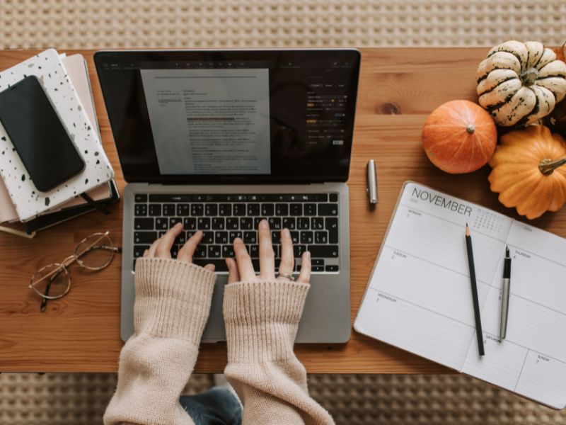 womans hands typing on a laptop with mini pumpkins in autumn aesthetic