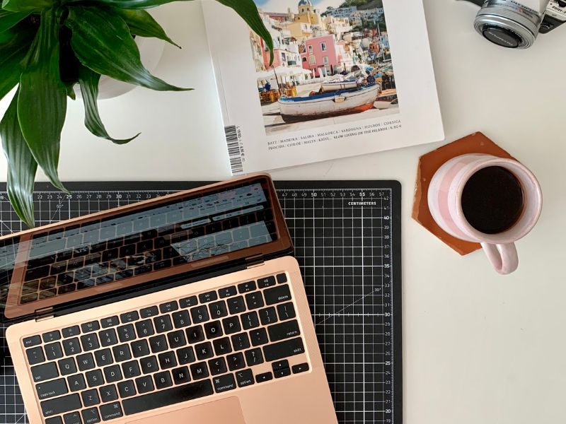 workspace setup with a laptop, coffee, a plant, and diary
