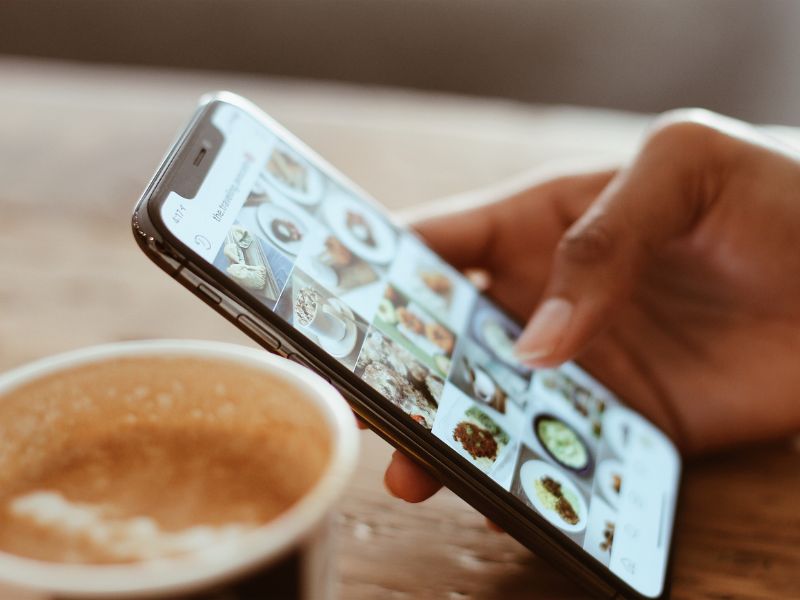 hand holding phone scrolling on social media with a cup of coffee in the frame.
