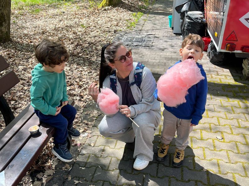 woman between two little boys holding cotton candy crouched down.
