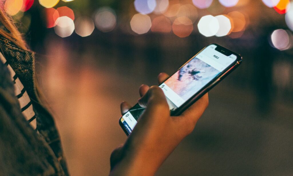 Woman holding phone at night with blurred lights in the background.