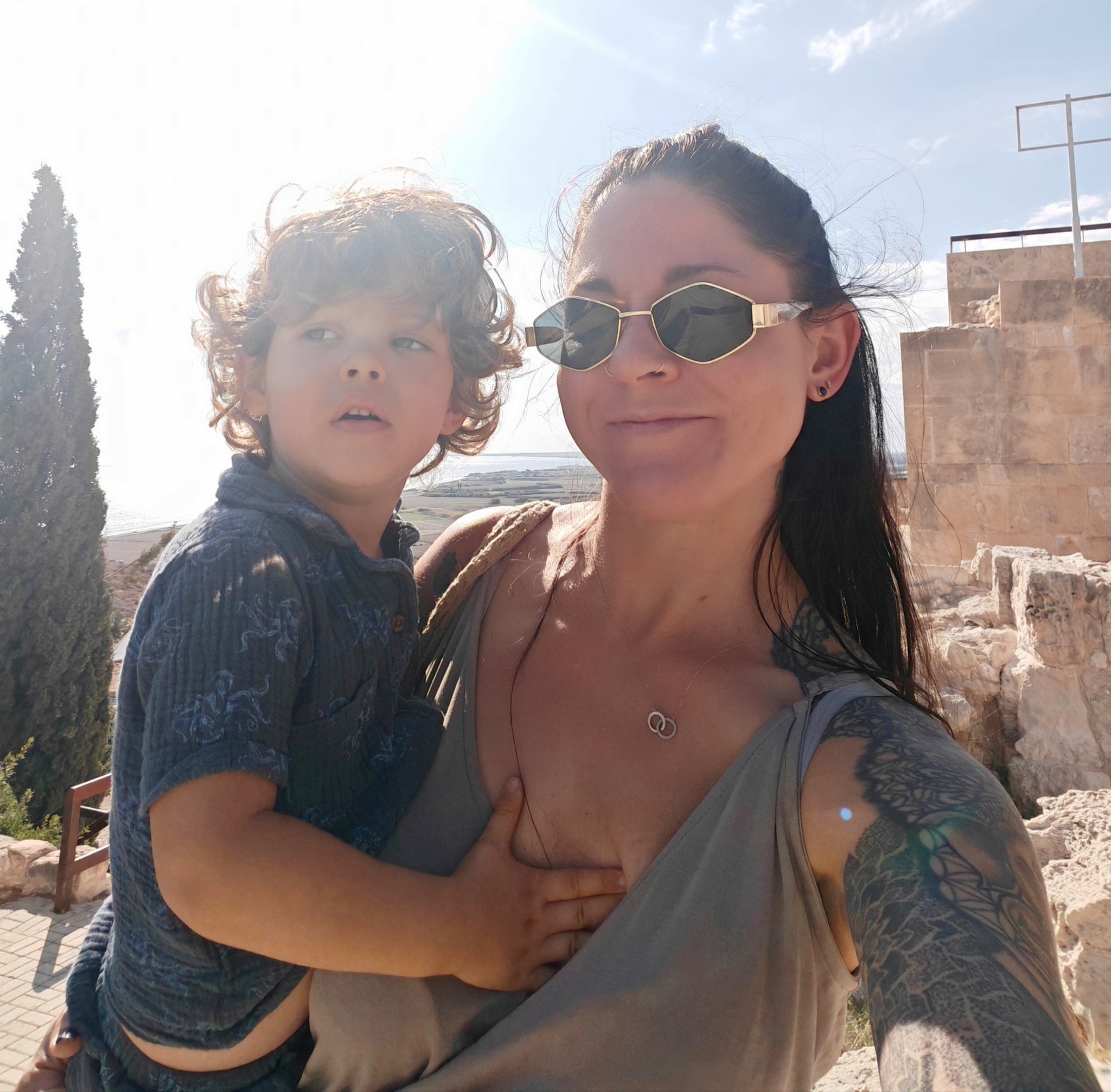 Jade Janosi smiling and holding her curly-haired toddler, who is wearing hexagonal sunglasses