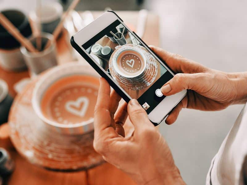 womans hands with cell phone taking a picture of latte art for social media content strategy