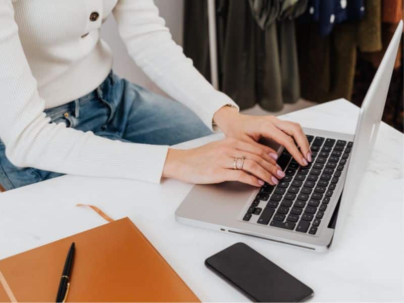 faceless woman typing on a macbook doing email marketing for digital products