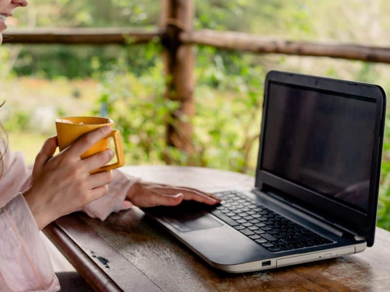 faceless woman on laptop in a cabin holding coffee mug studying digital product pricing strategy